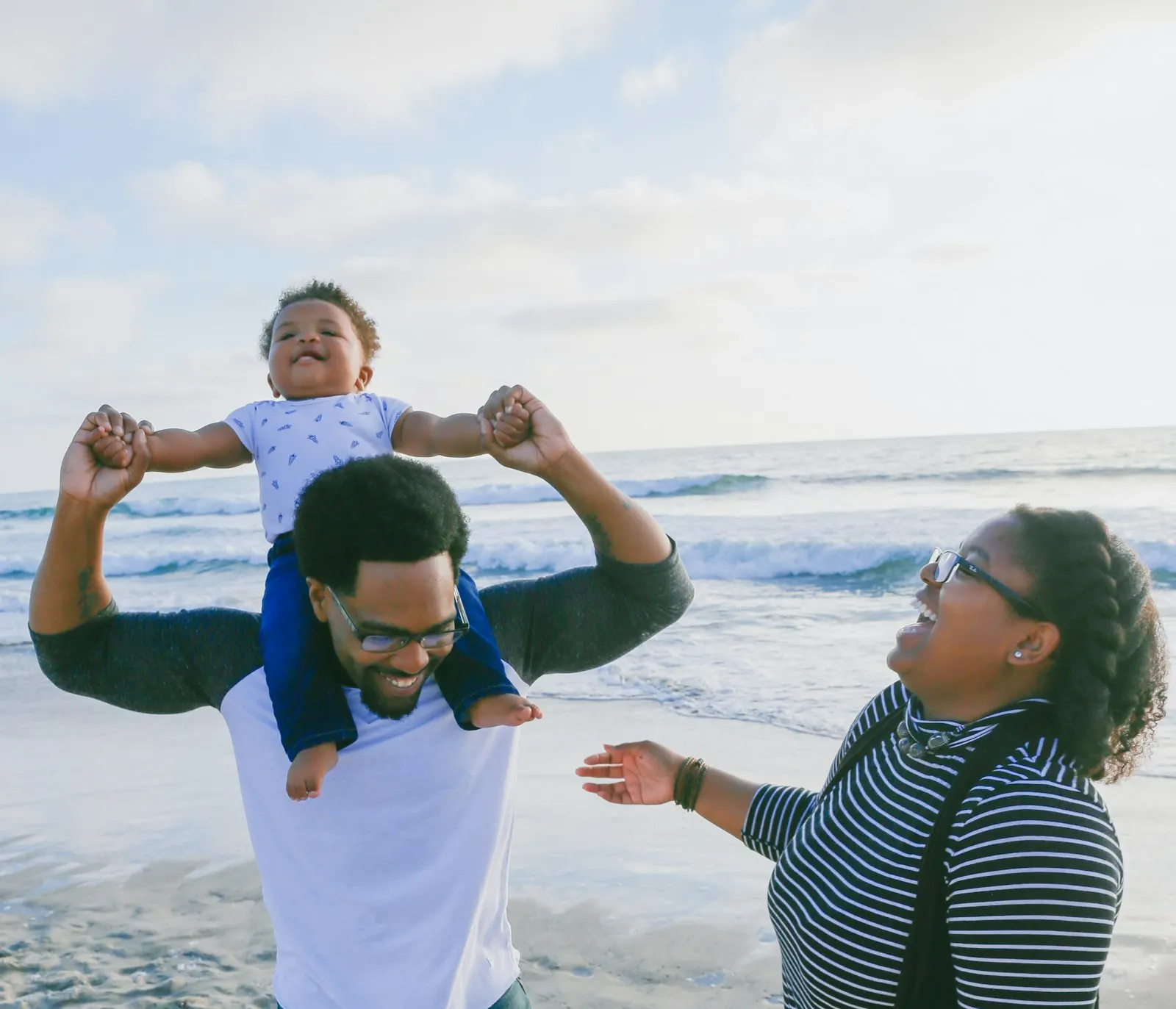 Father carrying his young daughter on his shoulders at the beach while mother smiles
